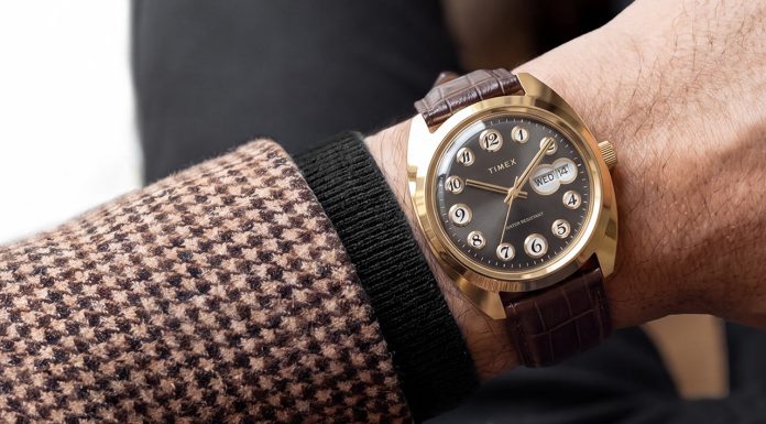 Timex 1976 Rotary Phone Dial Reissue: tárcsás telefon a csuklón Timex® 1976 Rotary Phone Dial Reissue with a gold-tone case, black dial, and brown leather strap worn on the wrist with a patterned blazer.