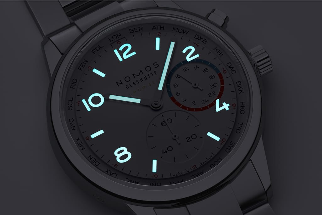 Close-up of a NOMOS Club Sport neomatik Worldtimer watch dial with glowing blue numerals and city ring.