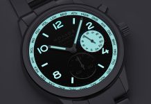 Nomos Club Sport Neomatik Worldtimer Dark: világidő fekete számlapon, teljes fényerővel Close-up of a NOMOS watch face with turquoise bezel ring showing city codes, black dial, cyan luminescent numerals and hands, metal bracelet.