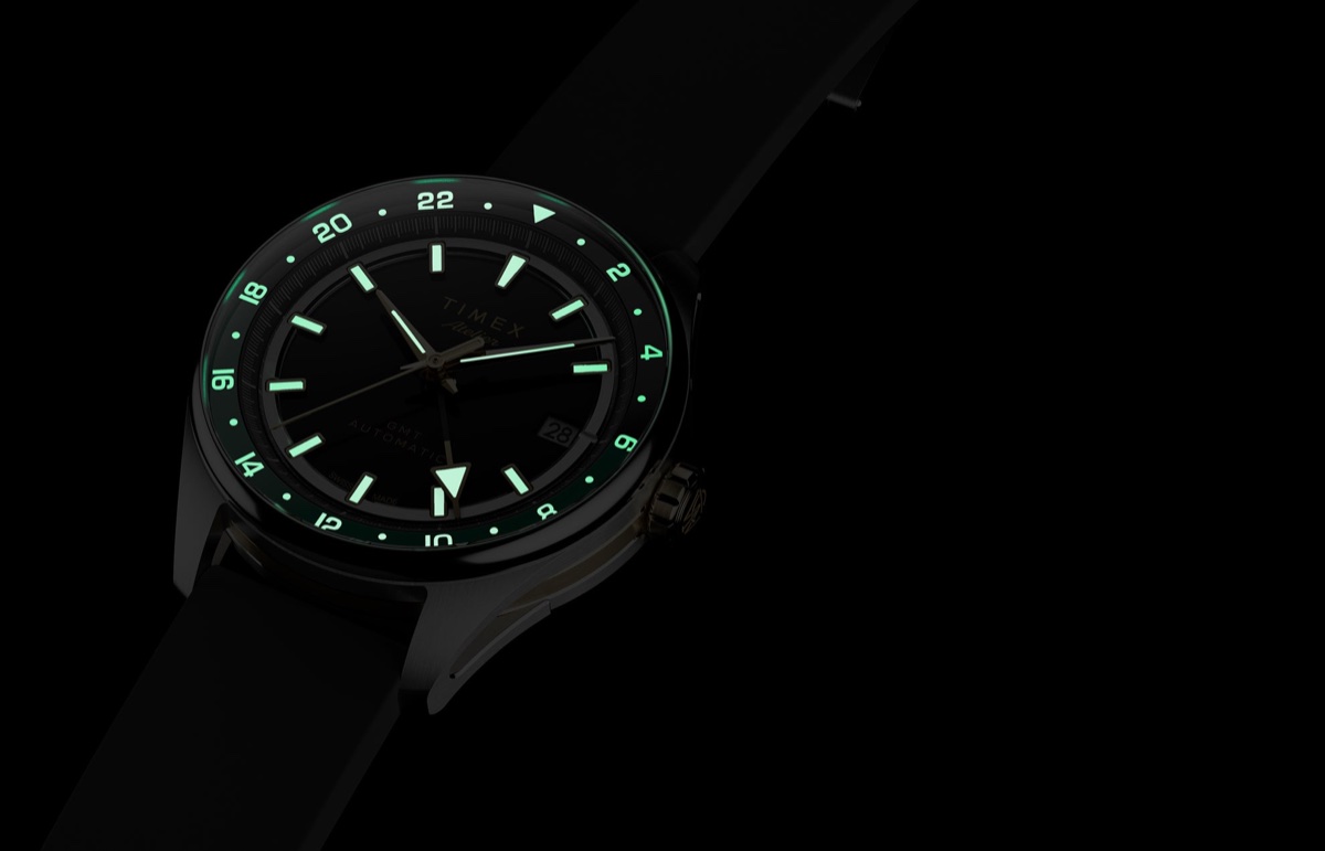 Timex Atelier GMT Première M1a: 38 milliméterben tér vissza a márka GMT-je Timex Atelier GMT Première M1a watch glowing in the dark with illuminated hands, hour markers, and 24-hour scale.