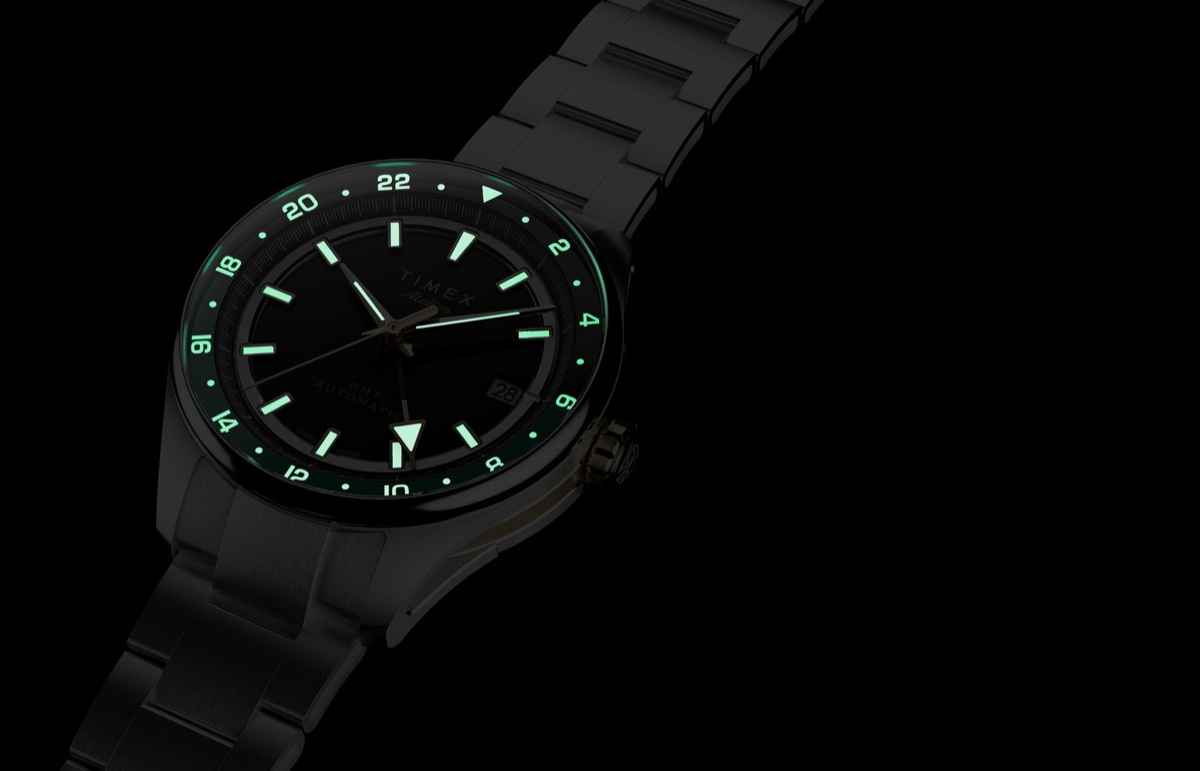 Timex Atelier GMT Première M1a: 38 milliméterben tér vissza a márka GMT-je Timex Atelier GMT Première M1a watch glowing in the dark with illuminated hour markers, hands, and 24-hour scale.