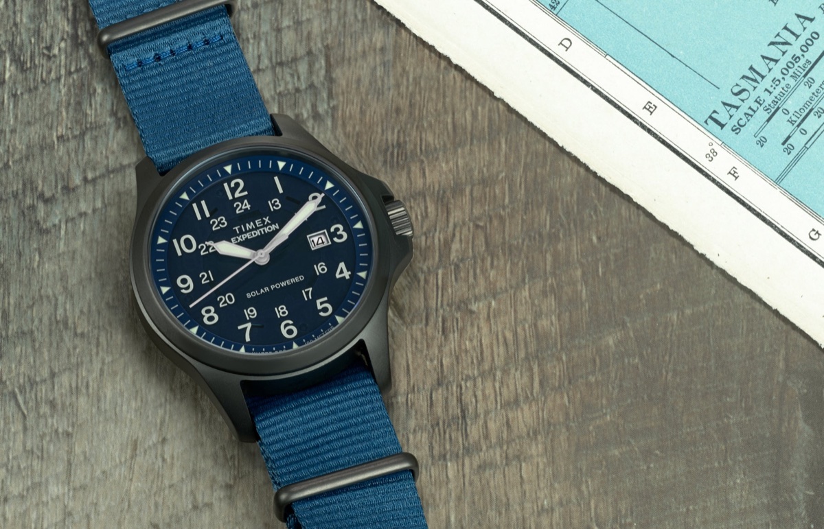 Timex túraóra-útmutató: mi számít tényleg a terepen, és mi csak funkciólista Expedition Field Post Solar watch with blue dial and strap on map background – Timex Expedition® Field Post Solar watch featuring a deep blue dial, white numerals, and fabric strap, placed on a wooden surface next to a vintage map.