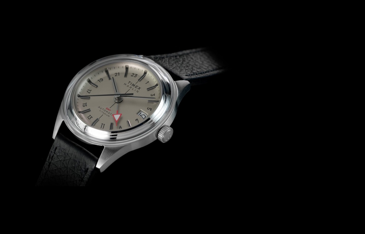 Timex Marlin Jet Titanium Automatic GMT: retrofuturisztikus tok, titánból Timex Marlin® Jet Titanium Automatic GMT watch with silver-tone titanium case, black leather strap, cream dial, red GMT hand, and date window on a black background.