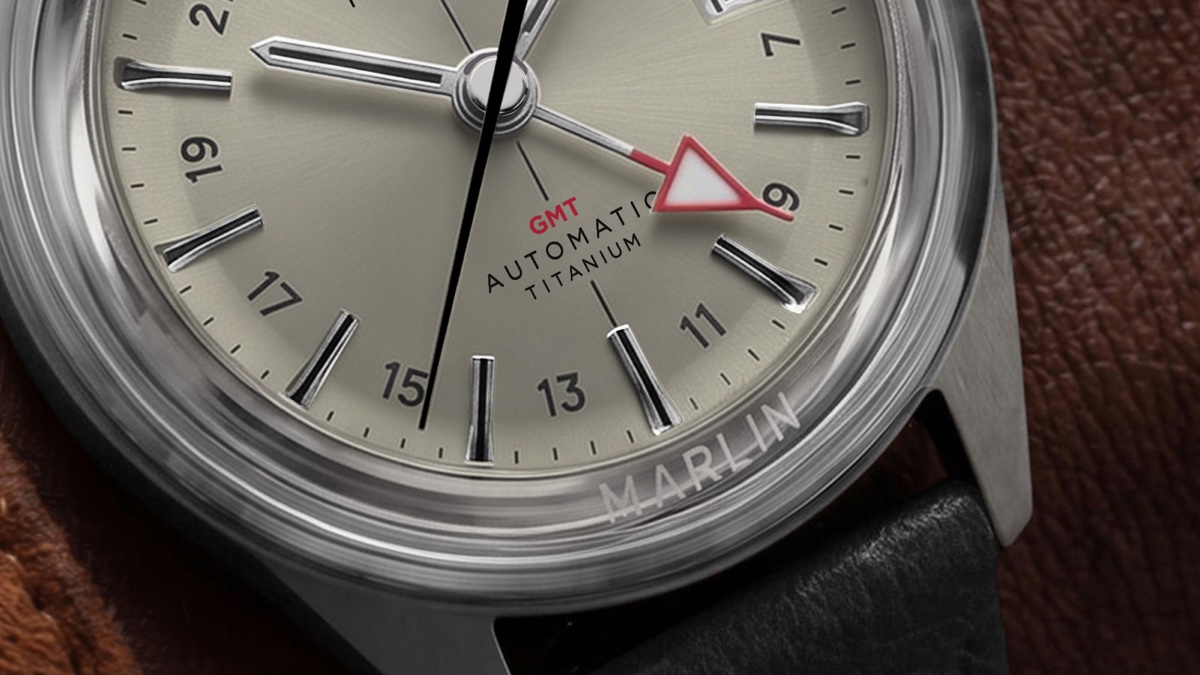 Timex Marlin Jet Titanium Automatic GMT: retrofuturisztikus tok, titánból Macro view of the Marlin® Jet Titanium Automatic GMT cream dial, highlighting the red GMT hand, applied hour markers, and Marlin branding on the crystal.