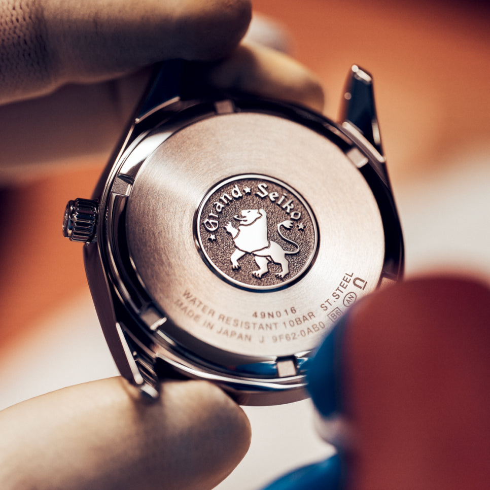 Grand Seiko óra hátlapja az oroszlános érmével, kézben tartva
