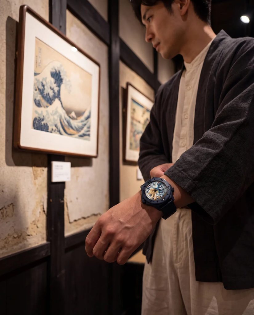 UNDONE Aquadeep The Great Wave - Visszatért és most aranyfüstre épül Hokuszai nagy hulláma Keresztbe tett karok egy bekeretezett Nagy hullám-nyomat előtt