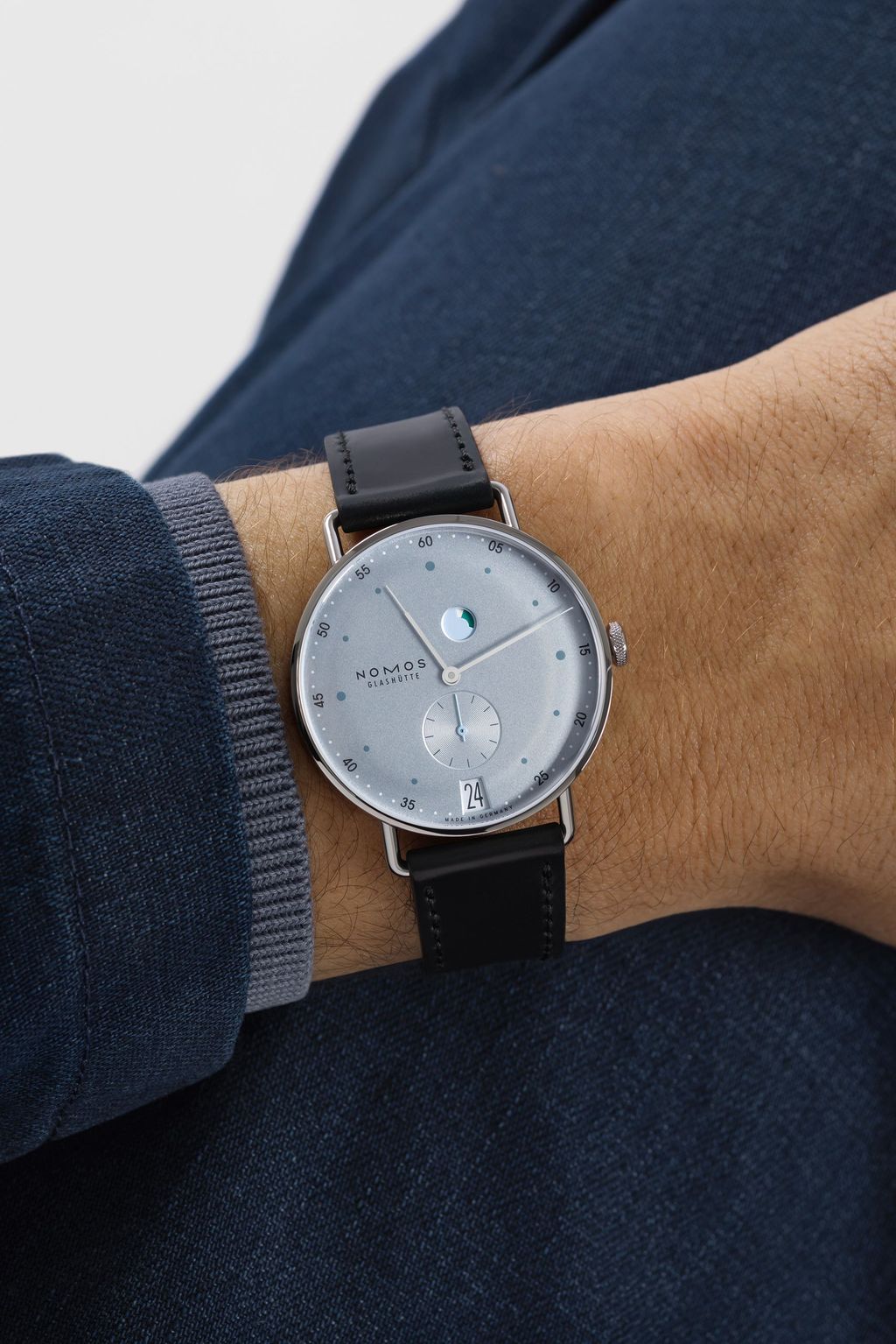 Jégkék Metro új kézi felhúzású kaliberrel: bemutatkozik a Nomos DUW 4701 Wrist shot of a Metro date power reserve watch with ice-blue dial and black strap.