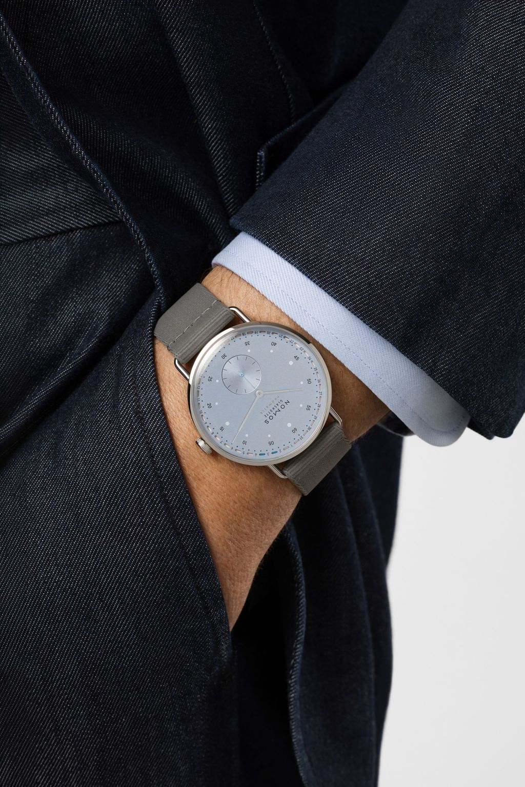 Jégkék Metro új kézi felhúzású kaliberrel: bemutatkozik a Nomos DUW 4701 Metro neomatik 41 Update watch with ice blue dial and gray fabric strap on a wrist, worn with a dark suit.