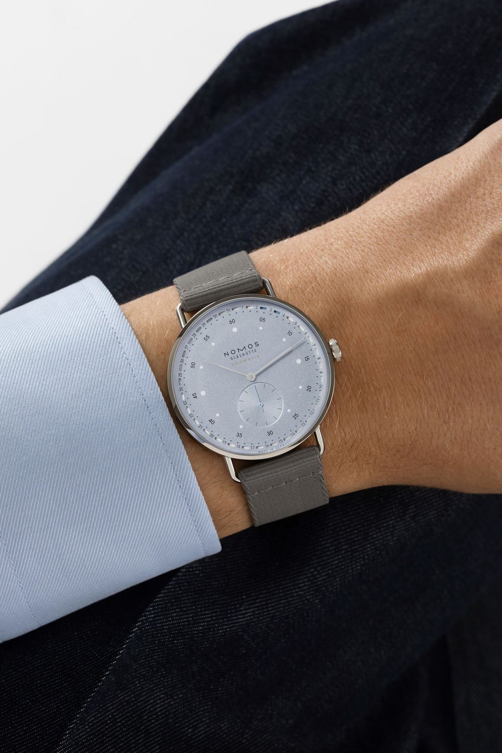 Jégkék Metro új kézi felhúzású kaliberrel: bemutatkozik a Nomos DUW 4701 Wrist shot of a NOMOS watch with ice blue dial and gray strap on a wrist.