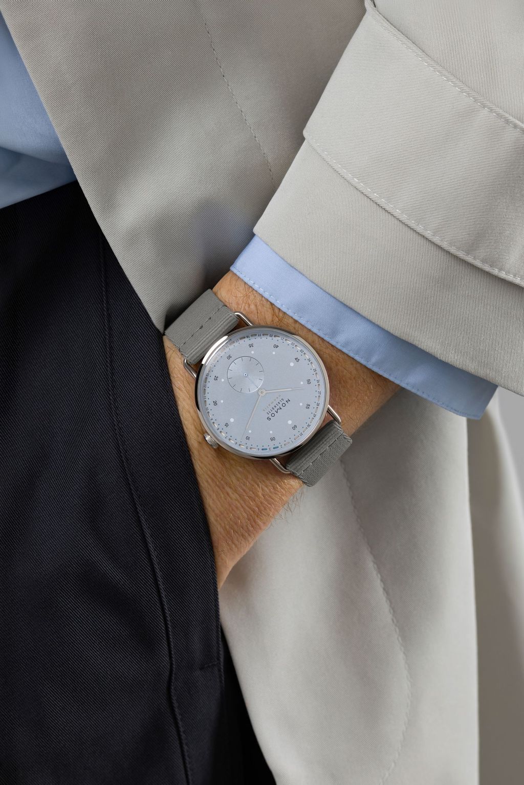 Jégkék Metro új kézi felhúzású kaliberrel: bemutatkozik a Nomos DUW 4701 NOMOS watch with ice blue dial and gray fabric strap on a wrist, partly covered by a light suit sleeve.
