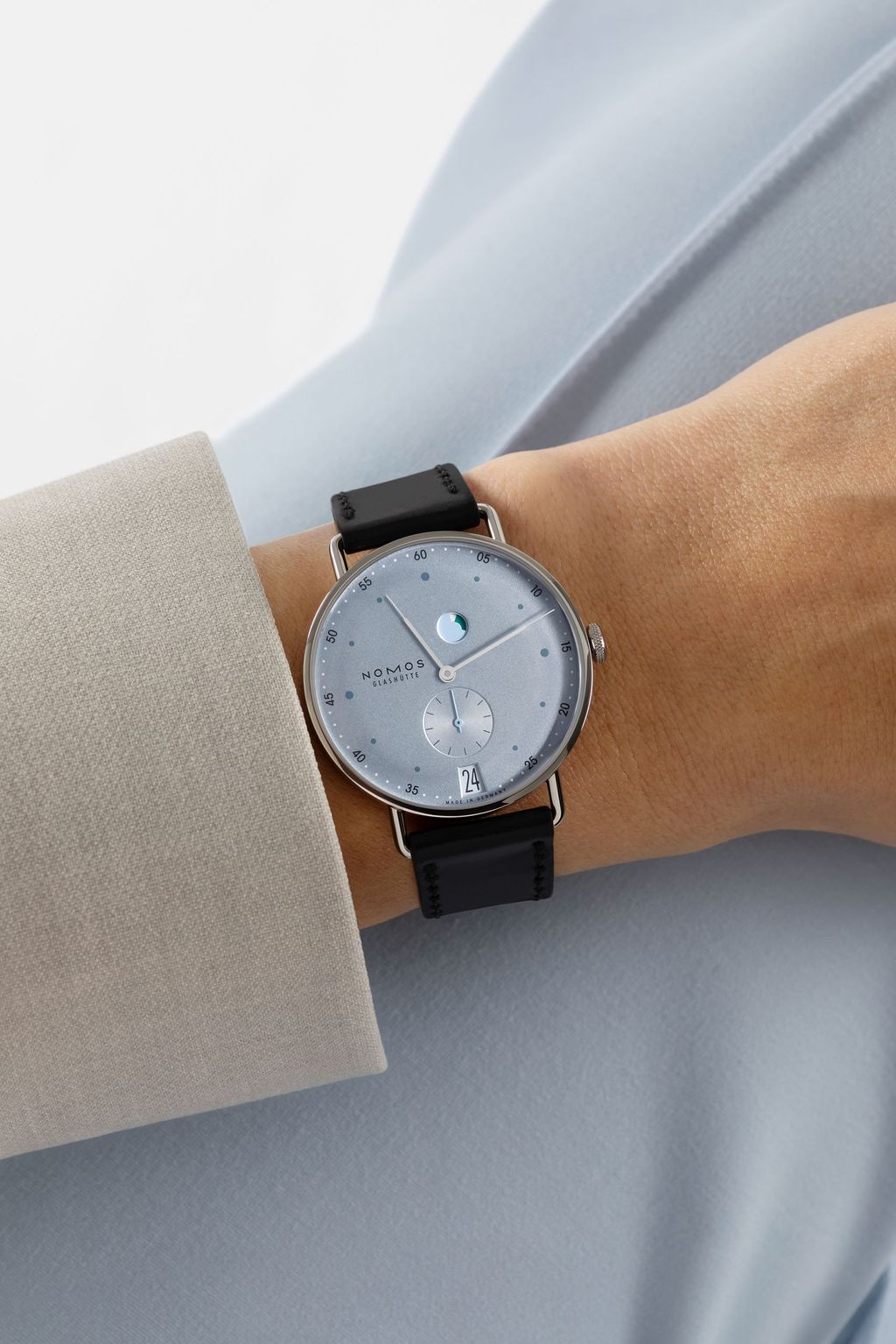Jégkék Metro új kézi felhúzású kaliberrel: bemutatkozik a Nomos DUW 4701 Wrist shot of a NOMOS watch with ice blue dial, black strap, date window and power reserve indicator.