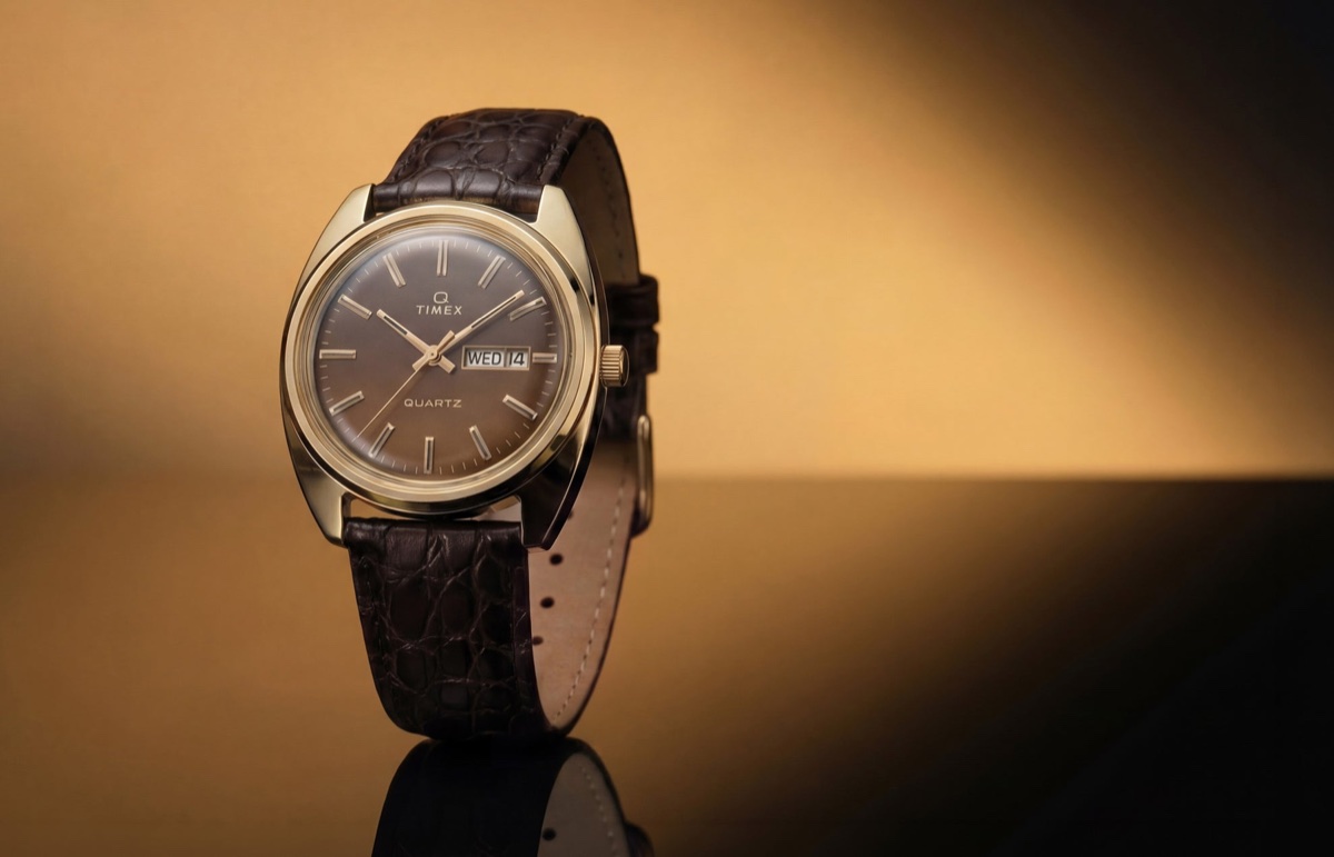TW2Y87200 Timex 1978 Day Date Fumé Reissue with a gold-tone case, brown gradient dial, and textured brown leather strap against a warm gold background.