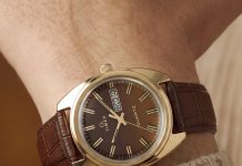 Timex 1978 Day Date Fumé Reissue: füstös barna számlap, 37 mm-es acéltok TW2Y87200 Wrist close-up of the Timex 1978 Day Date Fumé Reissue with a gold-tone case, brown leather strap, and day-date display.