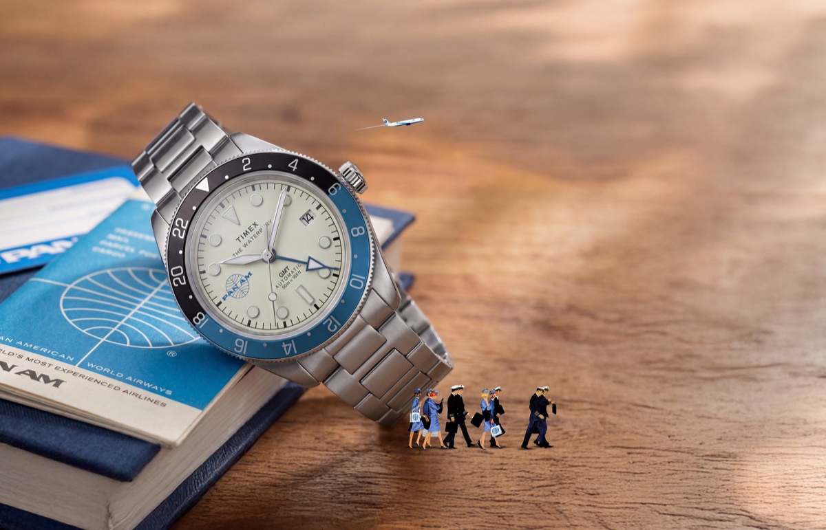 Pan Am x Timex Waterbury GMT: automata és kvarc változatban érkezik a két időzónás páros TW2Y94300 Pan Am x Timex Waterbury Automatic GMT watch beside a Pan Am travel book with miniature airline crew and airplane details.