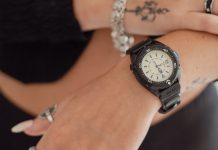 Feketébe öltözött a Timex Intrepid x Dimepiece: itt a 36 mm-es Blackout Edition TW6A19800 Timex Intrepid x Dimepiece ‘Blackout’ Edition with a cream dial and black strap, worn on a wrist beneath a hand with silver jewelry.