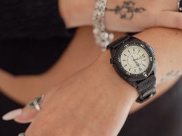 Feketébe öltözött a Timex Intrepid x Dimepiece: itt a 36 mm-es Blackout Edition TW6A19800 Timex Intrepid x Dimepiece ‘Blackout’ Edition with a cream dial and black strap, worn on a wrist beneath a hand with silver jewelry.