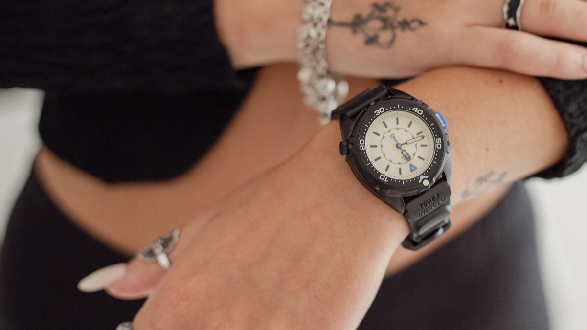 Feketébe öltözött a Timex Intrepid x Dimepiece: itt a 36 mm-es Blackout Edition TW6A19800 Timex Intrepid x Dimepiece ‘Blackout’ Edition with a cream dial and black strap, worn on a wrist beneath a hand with silver jewelry.